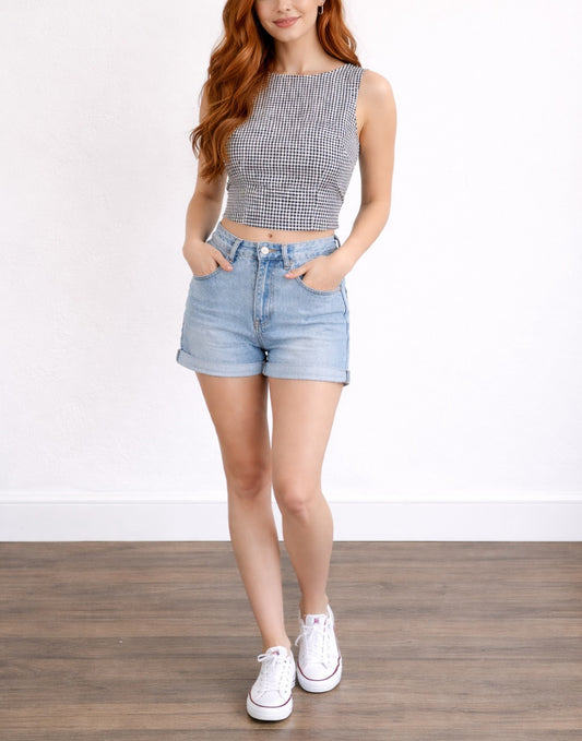 Woman wearing a checkered crop top and denim shorts on a white background