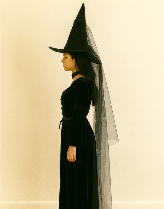 Side view of person wearing a black witch costume with a pointed Witch Hat and long dress on a beige background