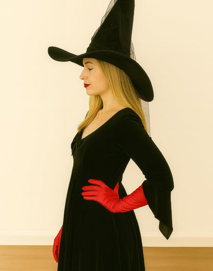 Side view of person wearing a black witch costume with a hat, dress, and red Witch Long Gloves on a plain background