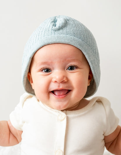 A baby wearing a white Baby Beanie.