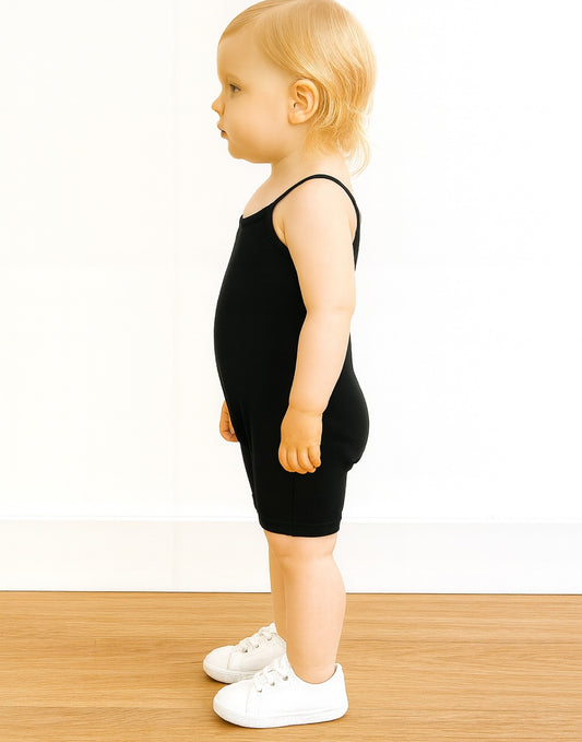 Side view of child wearing a black Cami Unitard Romper on a white background.