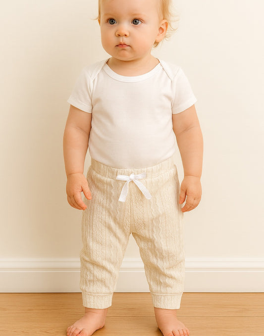 Baby wearing a white onesie and striped jogger pants against a plain background