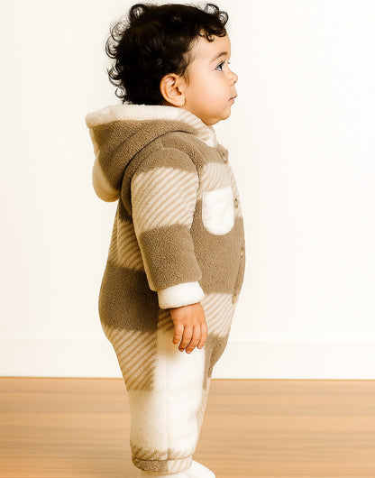 Side view of young child wearing a light brown and white plaid Patch Pocket Hooded Jumpsuit on wooden floor in front of a plain white wall.