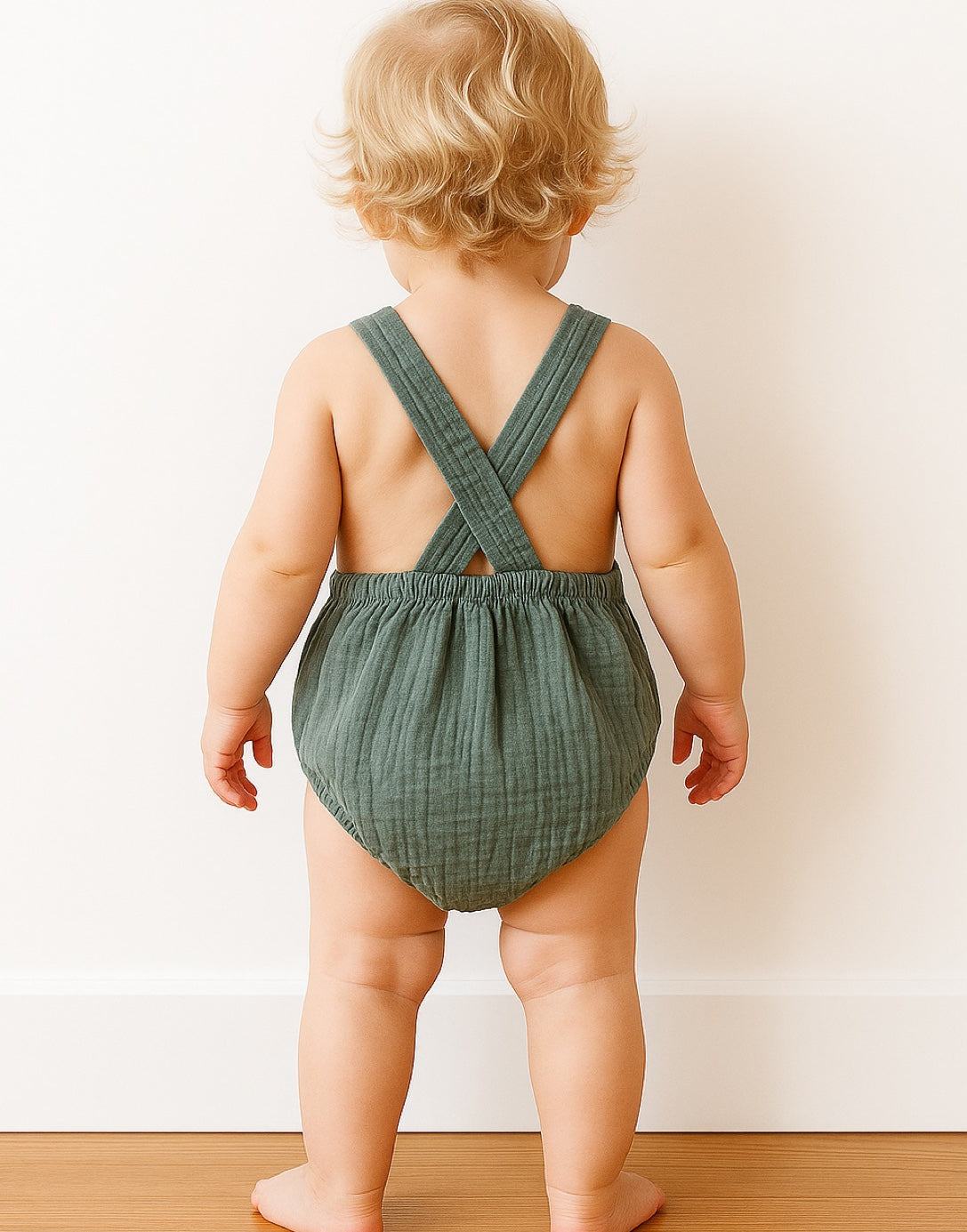 Back view of baby wearing a green Patch Pocket Overall Romper in front on a plain white background.