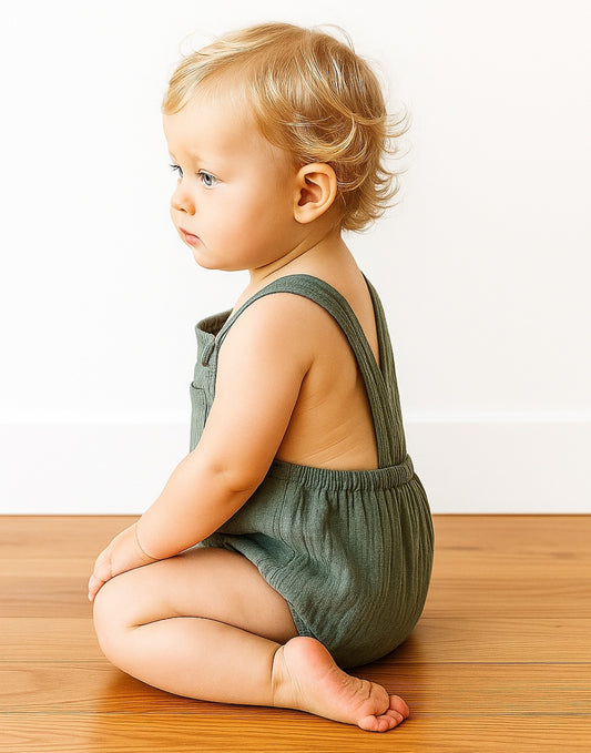 Side view of baby wearing a green Patch Pocket Overall Romper and sitting in front on a plain white background.