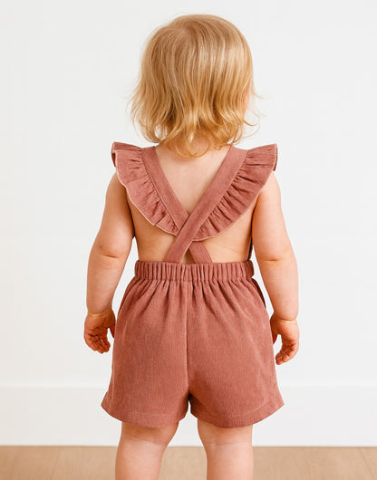 Back view of child wearing a pink romper with ruffled straps on a white background