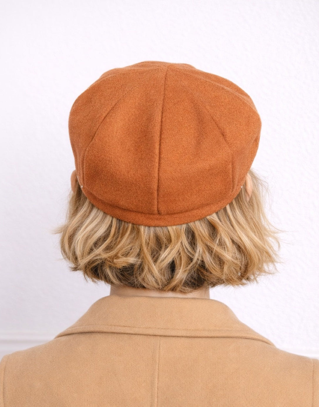 Back view of woman wearing a brown Baker Boy Cap and coat against a white background.
