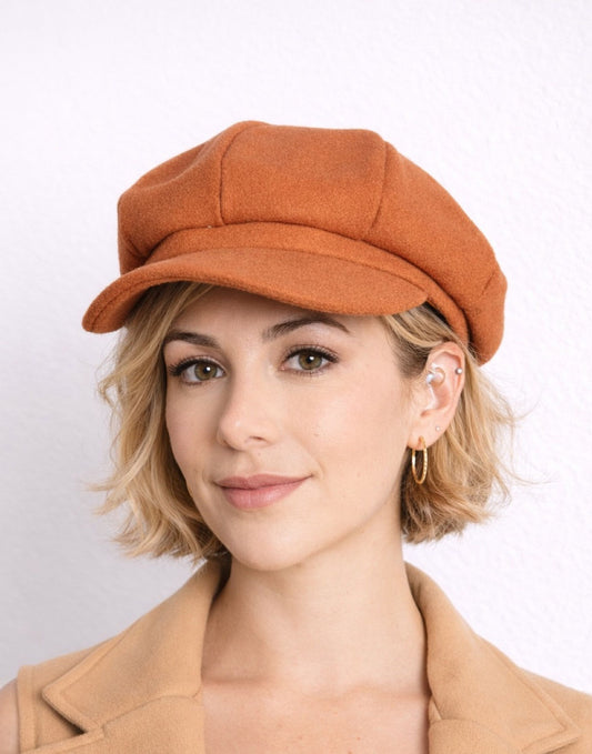 Woman wearing a brown Baker Boy Cap and coat against a white background