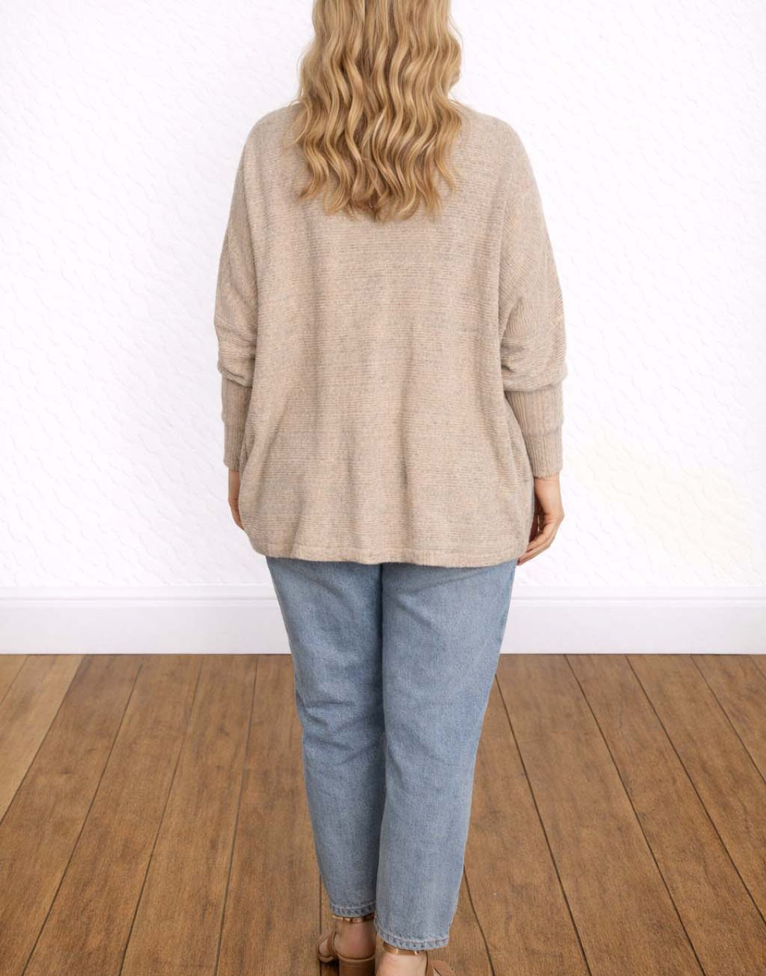 Back view of woman wearing a beige Batwing Sleeve Cardigan and blue jeans on a wooden floor.