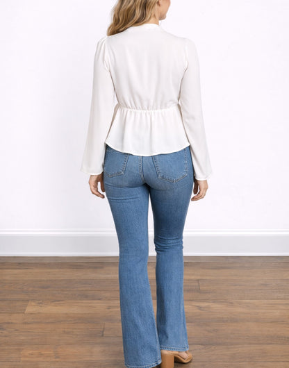 Back view of woman wearing a white Bell Sleeve Tie Front Peplum Top and blue jeans on a wooden floor with a white wall background.