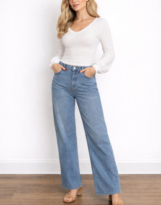 Woman wearing a white Bishop Sleeve Top and blue jeans against a white wall.