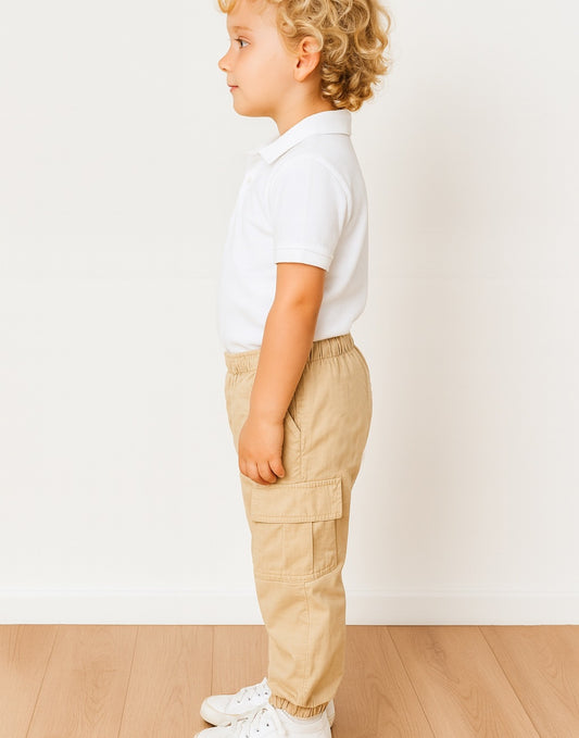 Side view of child wearing a white polo shirt and beige Cargo Pants standing on a wooden floor with a white wall background.