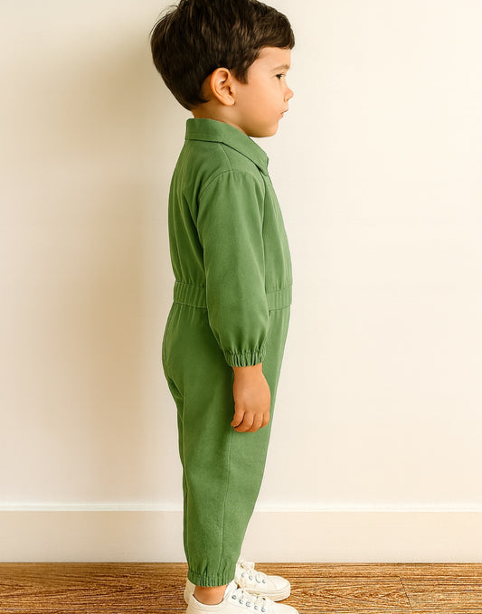 Side view of young boy wearing a green Cargo Utility Flightsuit Jumpsuit standing against a plain background.