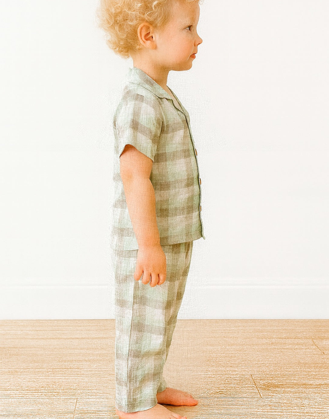 Side view of child wearing a green plaid pajama set against a white background.