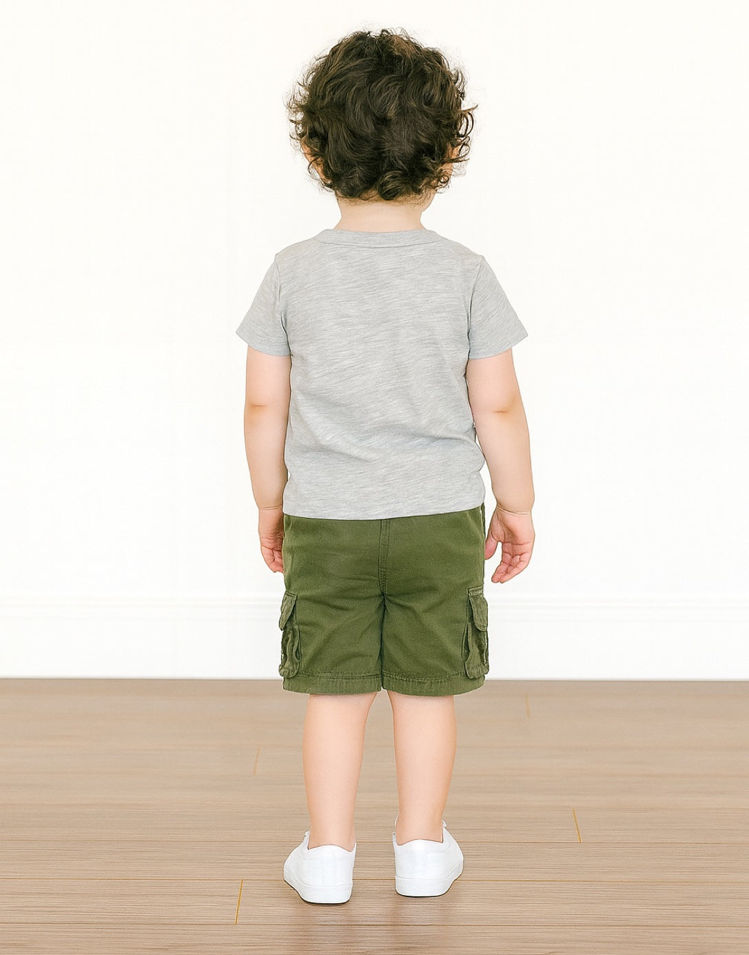 Back view of child wearing a gray T-Shirt and green cargo shorts on a white background