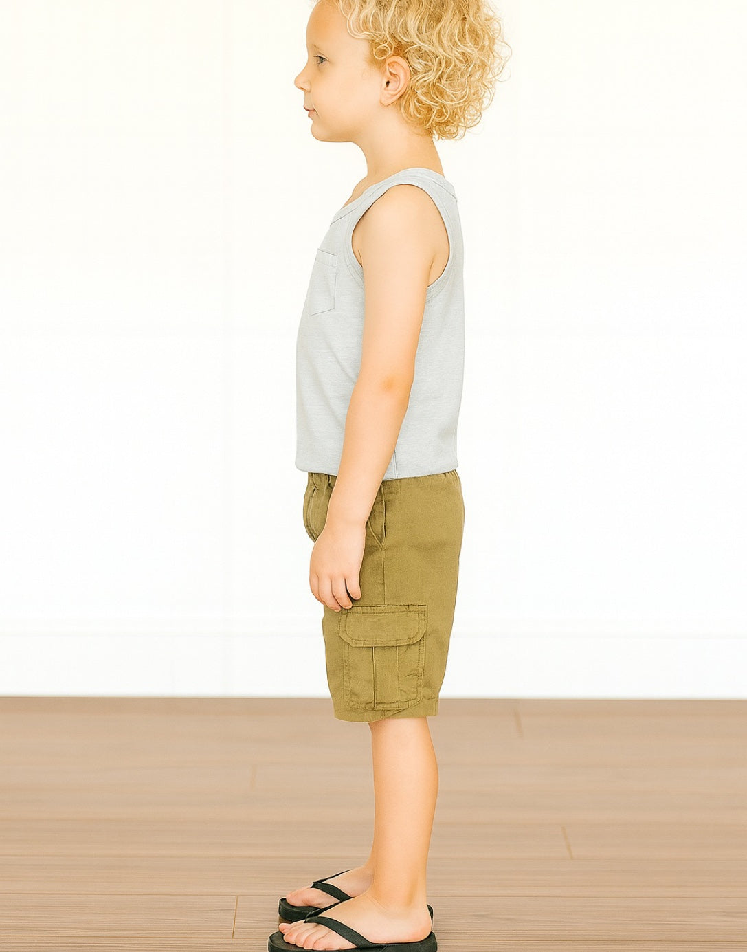 Side view of child wearing a gray Round Neck Pocket Tank Top and green shorts on a white background