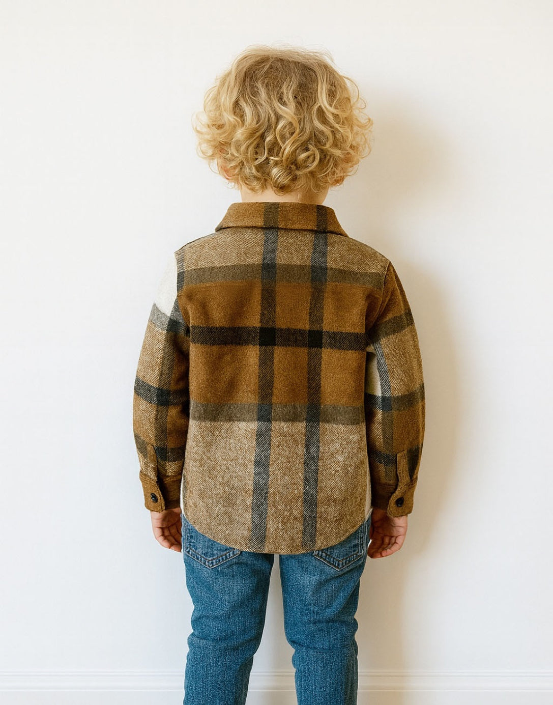 Back view of young boy wear brown and white plaid Shirt Jacket with denim jeans in front of plain white background.