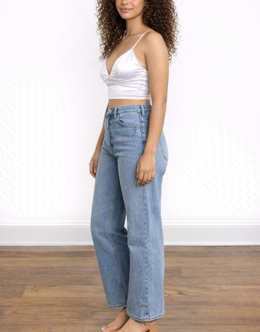 Side view of woman wearing a white Bralette Cami Top and blue jeans against a white wall.