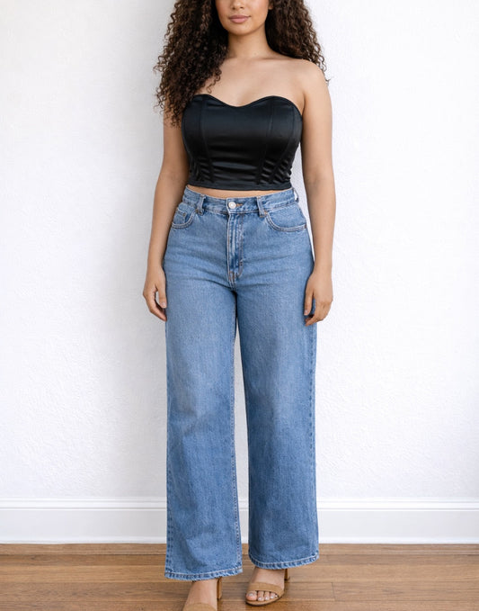 Woman wearing a black strapless Bustier Crop Top and blue jeans against a white wall.