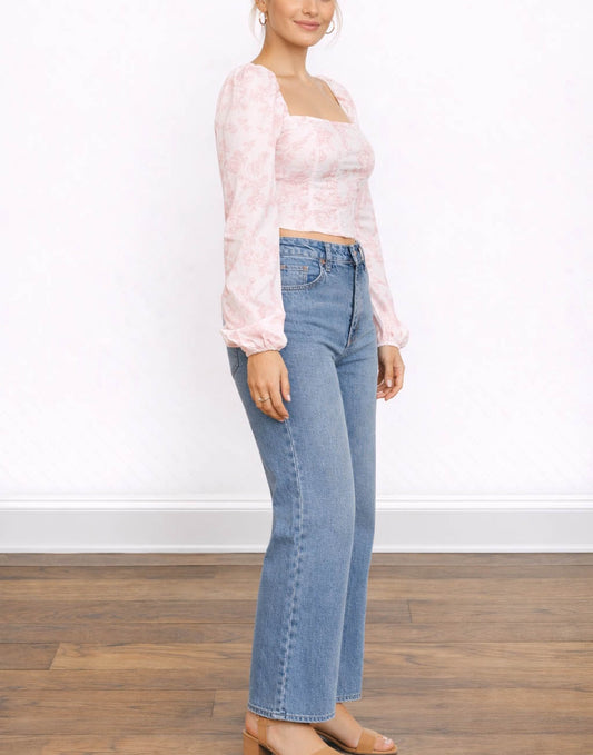 Side view of woman wearing a pink Bustier Long Sleeve Top and blue jeans on a white background.