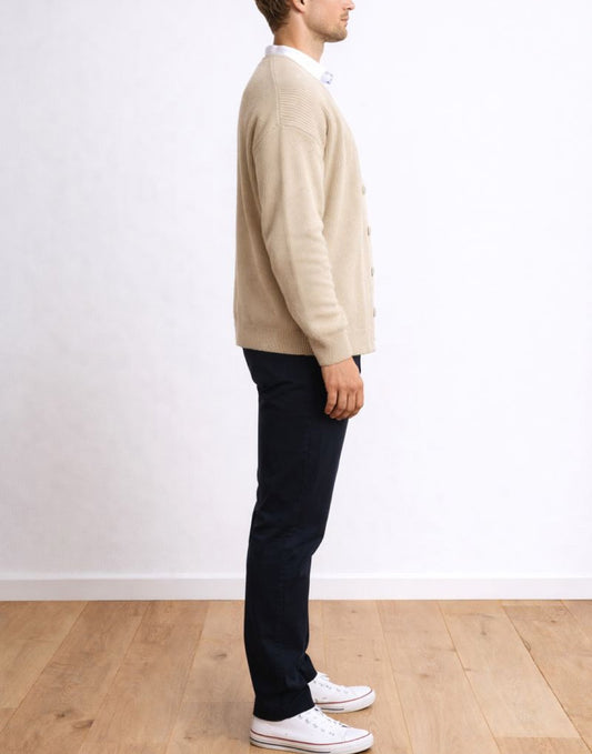 Side view of person wearing a beige Button Front Cardigan and black pants standing against a white wall.