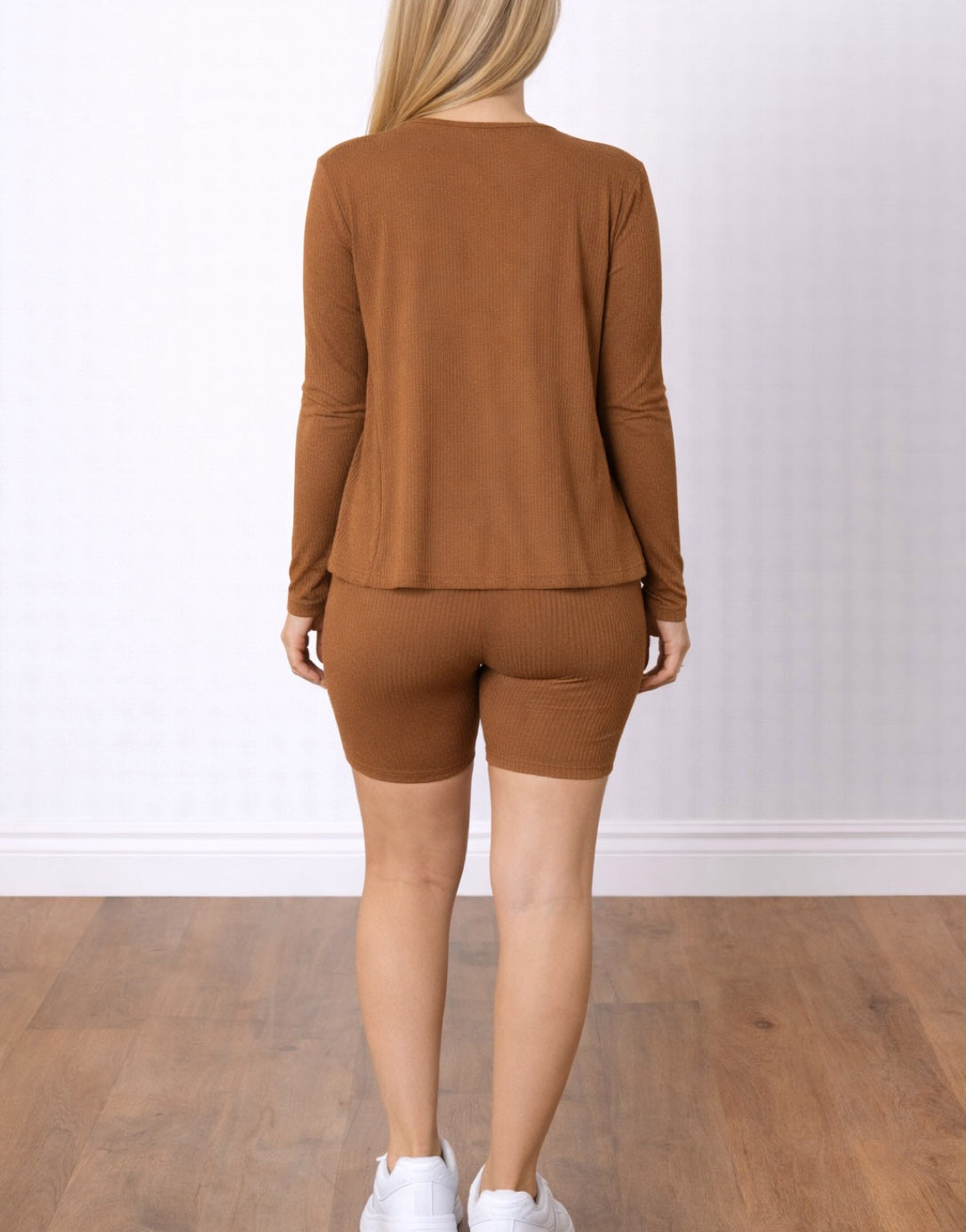 Back view of woman wearing a brown athletic outfit with a Cardigan, Crop Top and Biker Shorts on a white background.