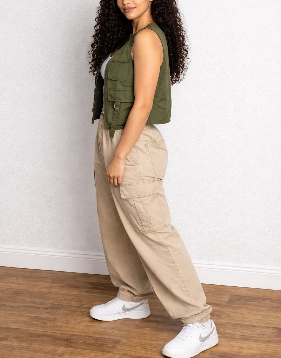 Side view of woman wearing a green Cargo Pocket Vest and beige cargo pants against a plain background.