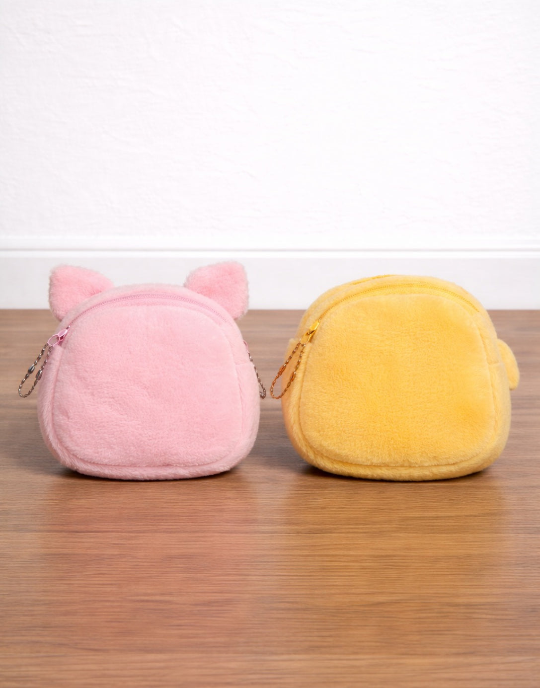 Back view of two plush coin purses, one pink and one yellow, on a wooden surface with a white background.