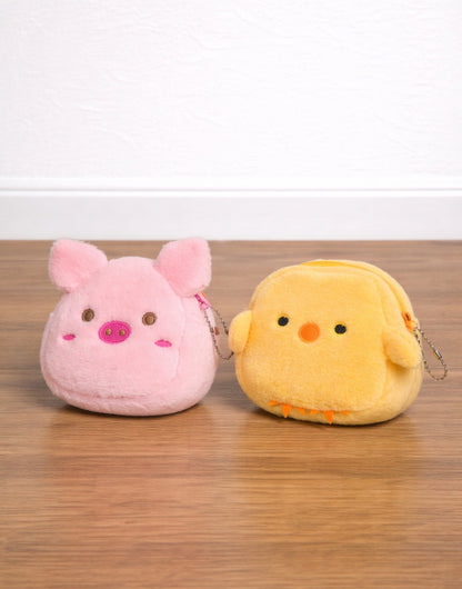 Side view of two plush Coin Purse, one pink pig and one yellow chick, on a wooden surface.