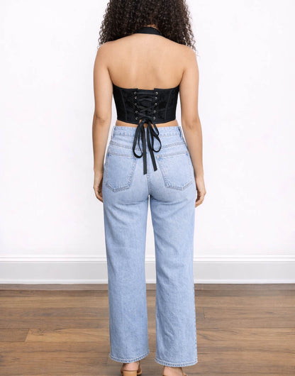 Back view of woman wearing a black sleeveless Corset Halter Top and light blue jeans on a white background.