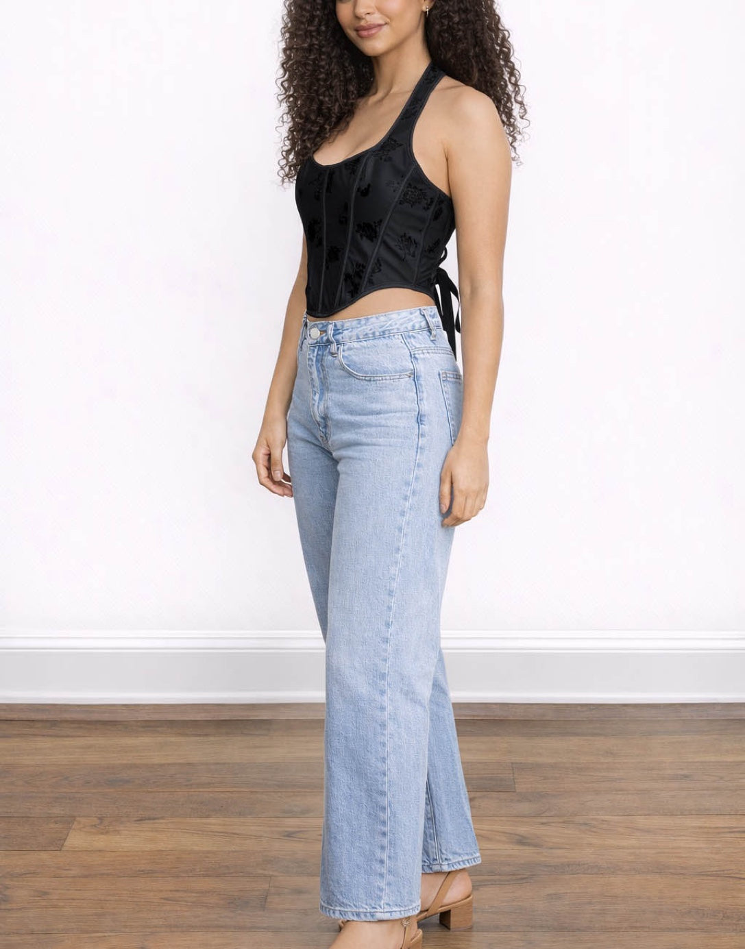 Side view of woman wearing a black sleeveless Corset Halter Top and light blue jeans on a white background.