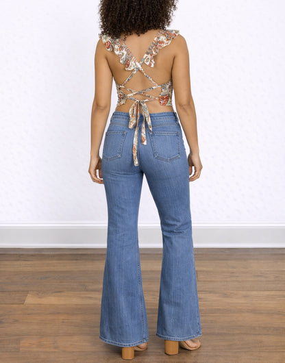 Back view of woman wearing a floral Crisscross Tie Back Ruffle Sleeve Crop Top and blue jeans on a white background.