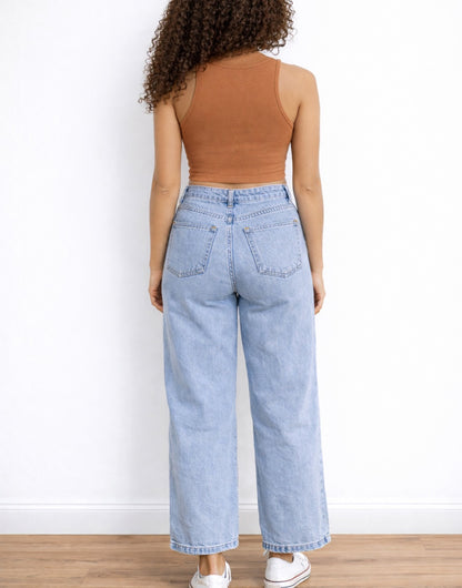 Back view of woman wearing a brown Crop Tank Top and light blue jeans against a white wall.