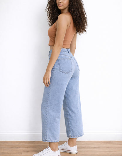 Side view of woman wearing a brown Crop Tank Top and light blue jeans against a white wall.