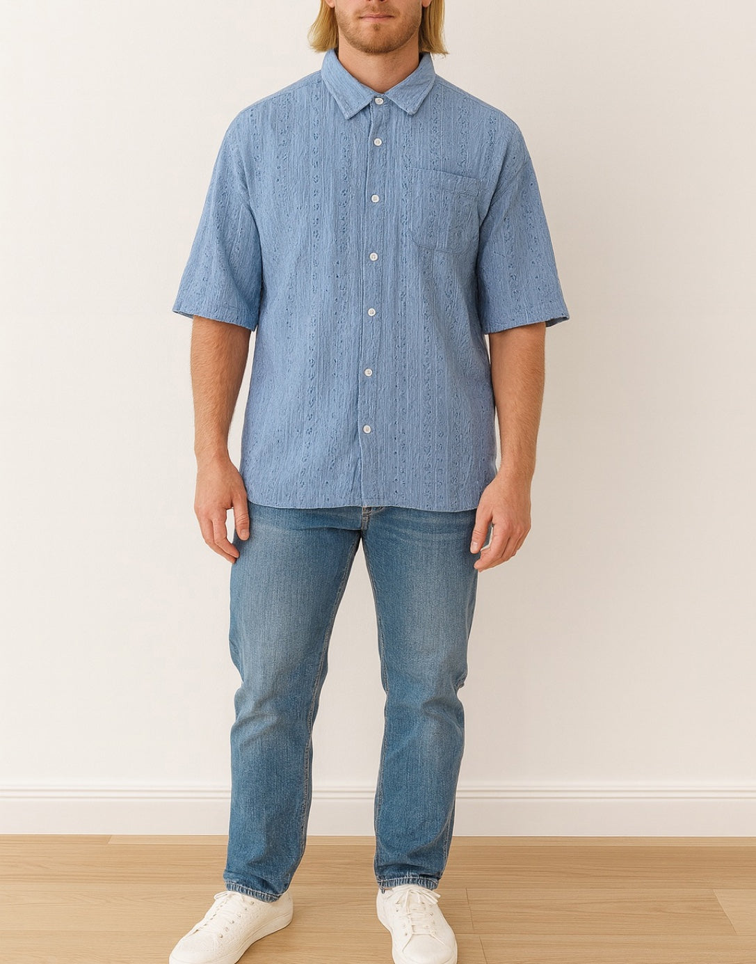 Man wearing a blue checkered Drop Shoulder Loose Fit Button Down Shirt and jeans standing against a white wall.