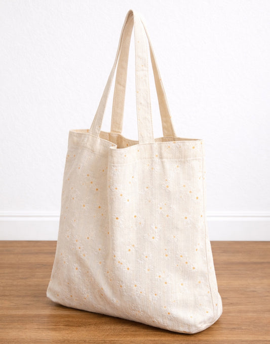 Side view of beige Tote Bag with subtle pattern on a wooden surface. 