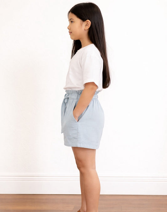 Side view of young girl wearing a white t-shirt and light blue Belted Patch Pocket Shorts against a plain background.