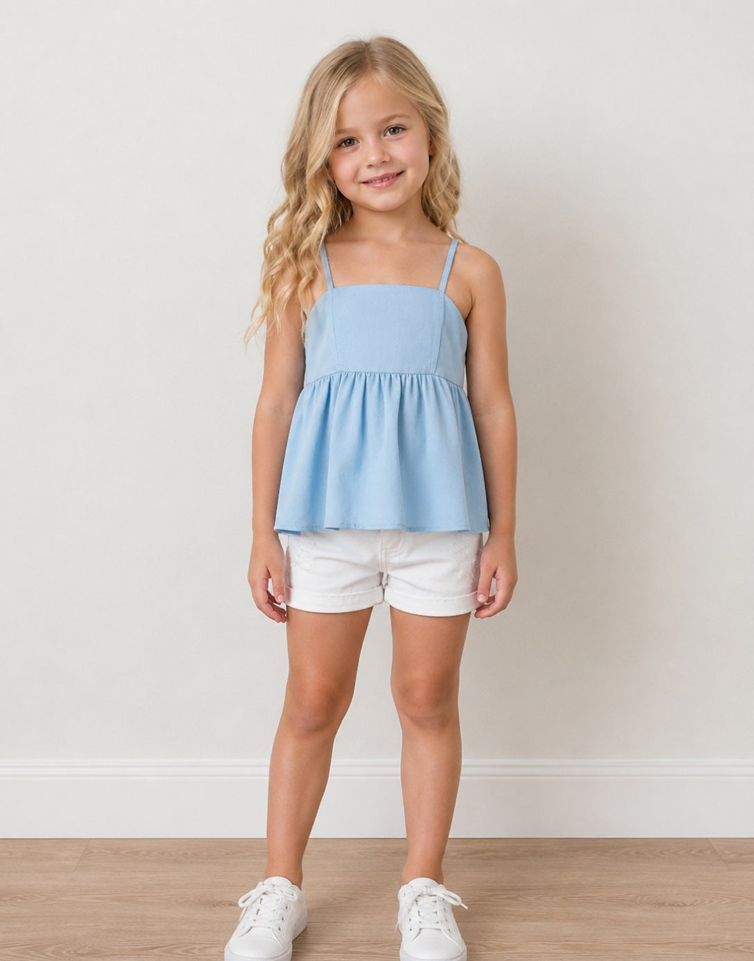 Young girl wearing a light blue Babydoll Cami Top and white shorts standing against a plain background