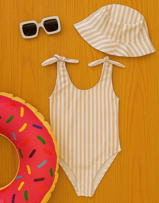 Back view of striped Bow Tie One Piece Swimsuit, sun hat, sunglasses, and inflatable ring on a wooden surface