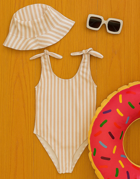 Striped Bow Tie One Piece Swimsuit, sun hat, sunglasses, and inflatable ring on a wooden surface