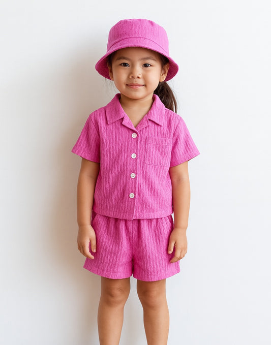 Child wearing a pink Button Front Shirt and Shorts Set with a matching hat on a white background