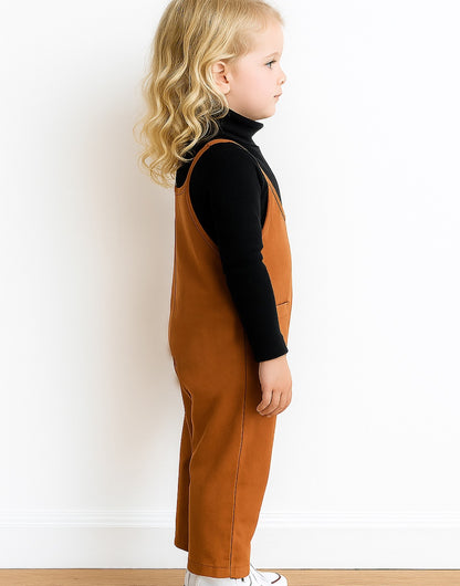 Side view of child wearing a brown overalls and black shirt against a white background.