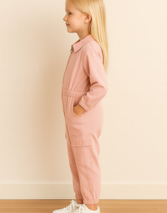 Side view of young girl wearing a pink Cargo Utility Flightsuit Jumpsuit against a plain background.