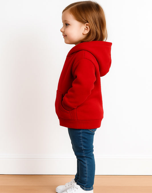 Side view of young girl wearing a red hoodie and blue jeans standing on a wooden floor with a white wall background