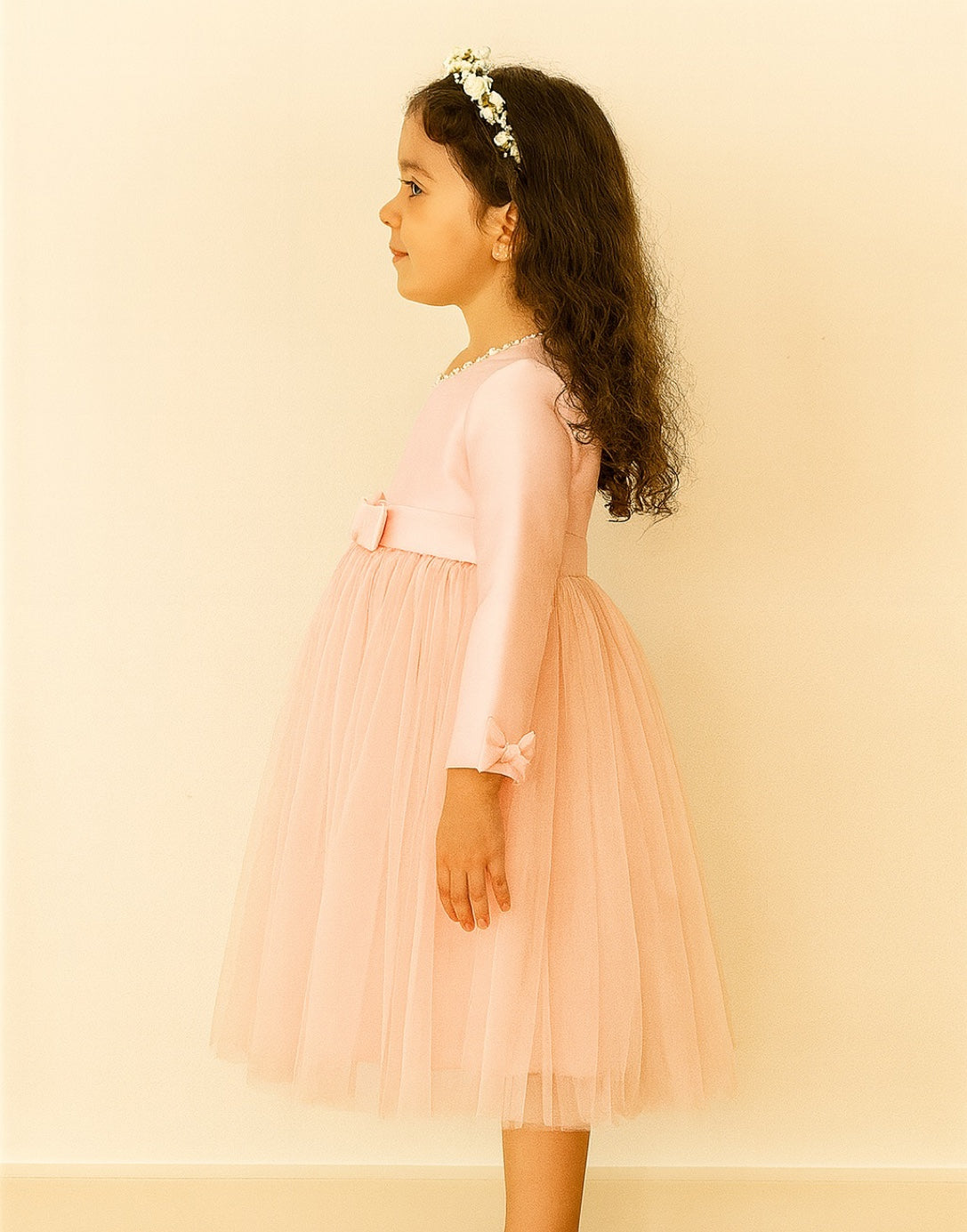 Side view of young girl wearing a pink Long Sleeve Princess Tulle Party Dress with a bow on a beige background.