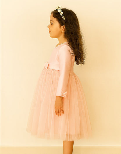 Side view of young girl wearing a pink Long Sleeve Princess Tulle Party Dress with a bow on a beige background.