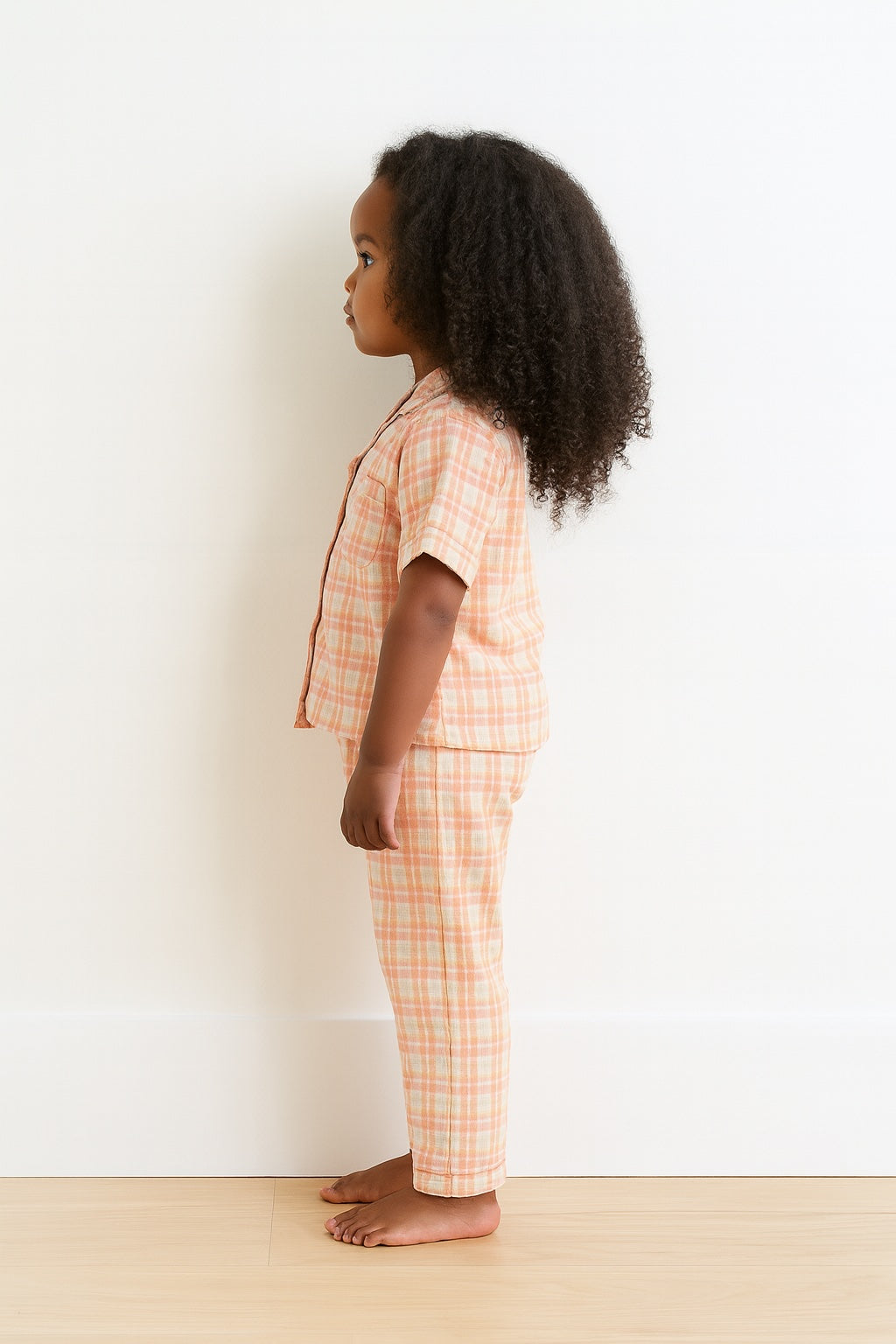 Side view of child wearing a pink plaid pajama set against a white background.