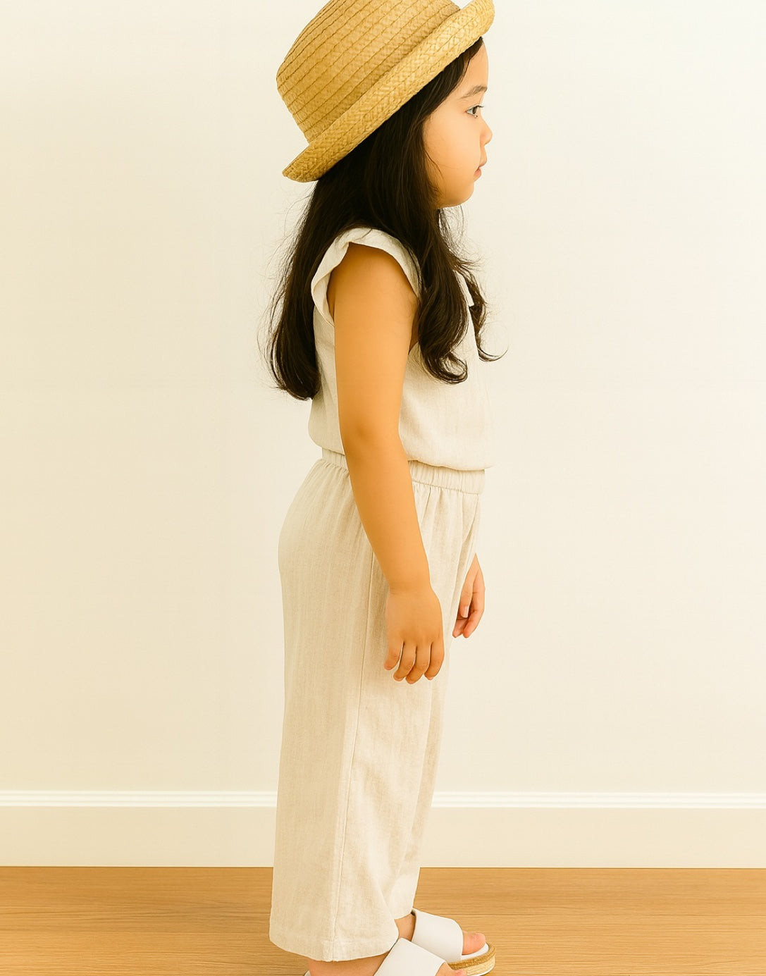 Side view of young girl wearing a beige ruffle top and Palazzo Pants with a matching hat against a plain background