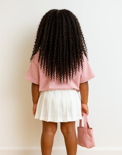 Back view of young girl in a pink shirt and white Elastic Waist Pleated Skirt holding a pink bag against a plain background.