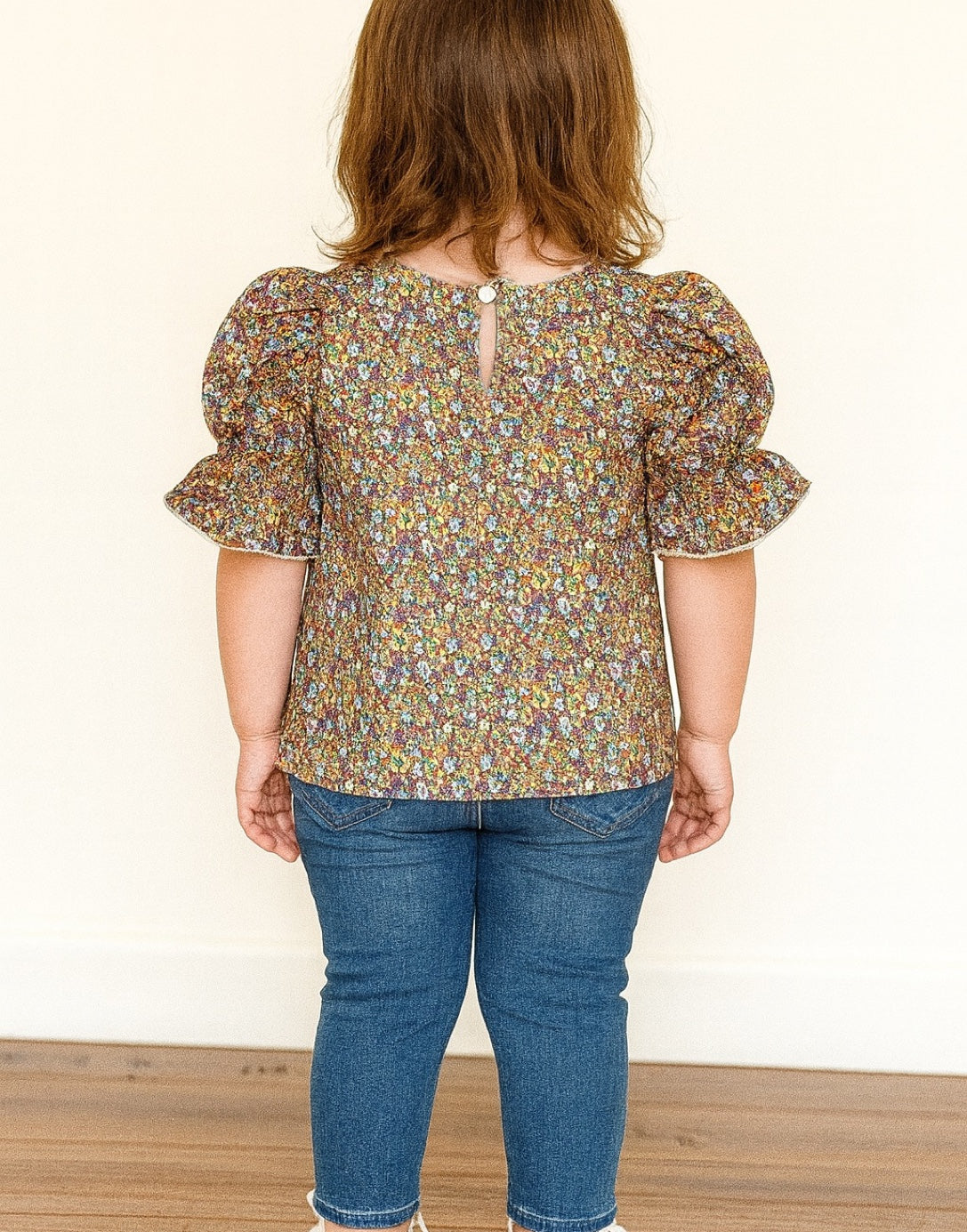 Back view of Puff Sleeve Blouse child wearing a floral blouse and blue jeans against a plain background